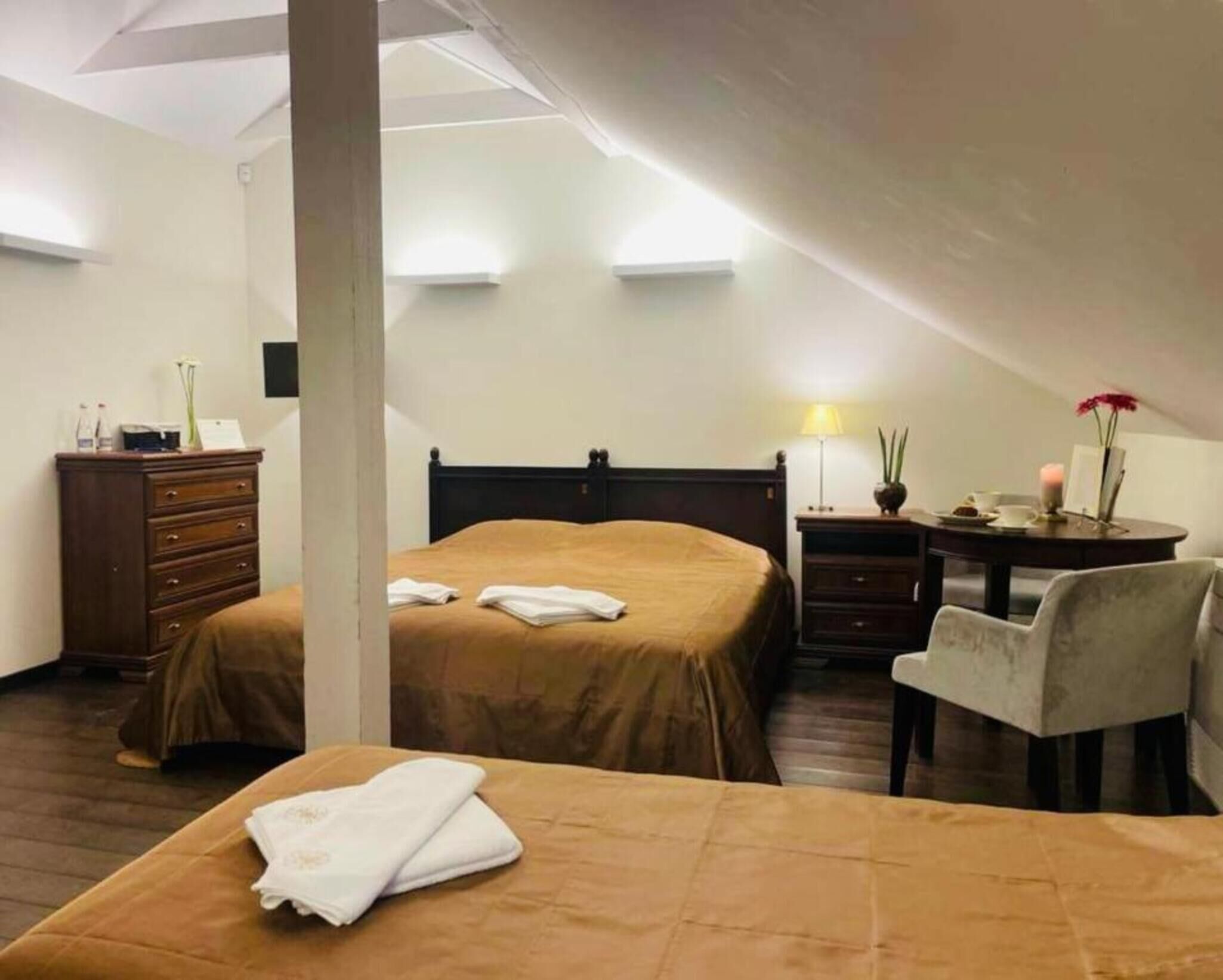 A hotel room with two beds, a desk, a chair, a dresser, and a lamp.