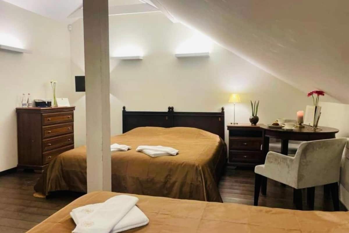 A hotel room with two beds, a desk, a chair, a dresser, and a lamp.