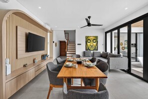 Una sala de estar moderna con una pared de acento de madera, un televisor de pantalla plana, una mesa de comedor con sillas, un sofá y un cuadro grande de Buda.