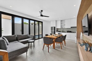 Un espacio habitable moderno con sofá, mesa de comedor, sillas, área de cocina y televisor.