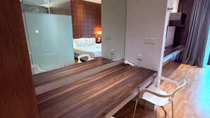 Een moderne hotelkamer met een houten bureau, een grote spiegel en een bed met witte lakens.