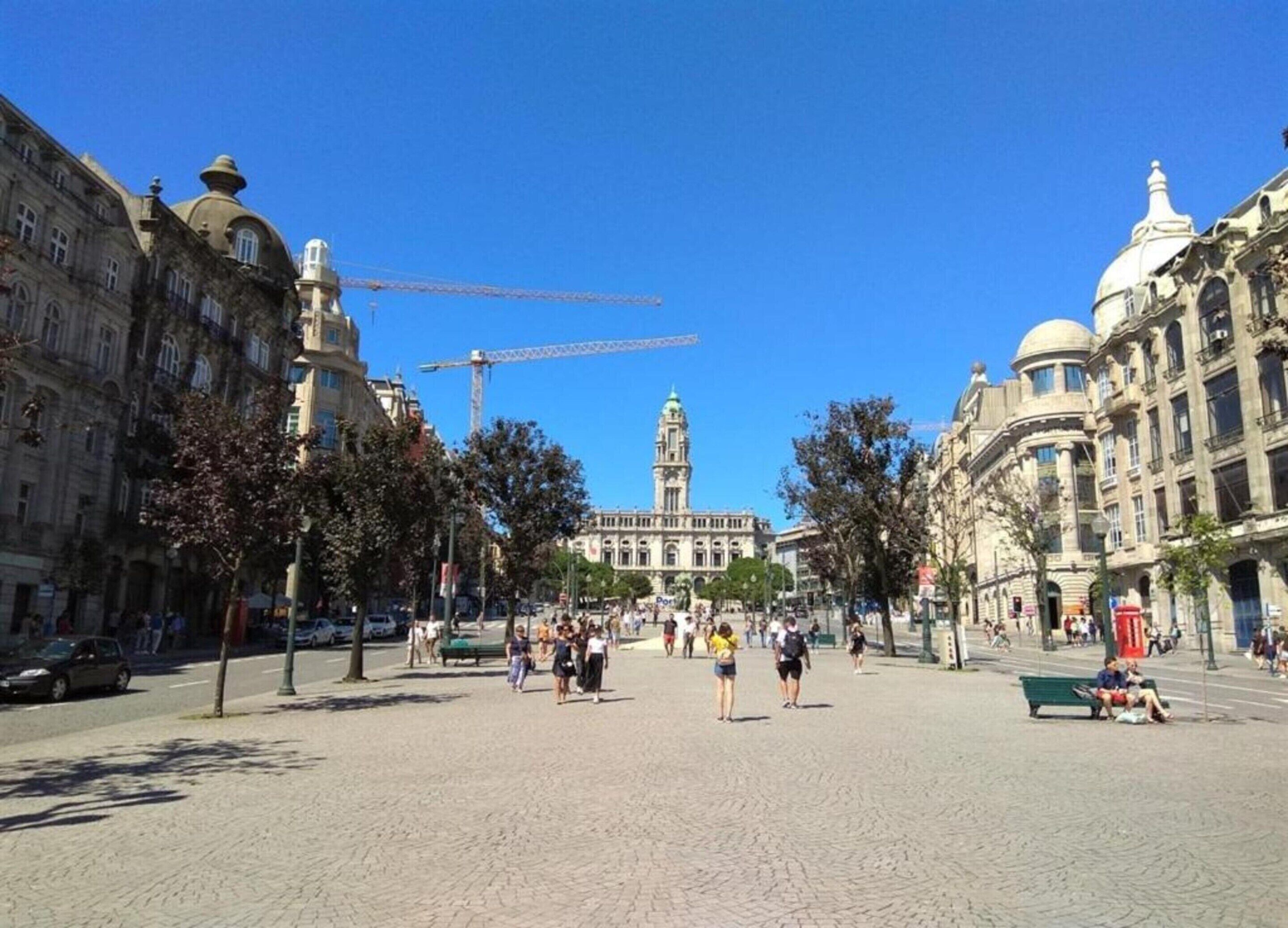 A public square with historic buildings, a prominent clock tower, and a construction crane in the background.