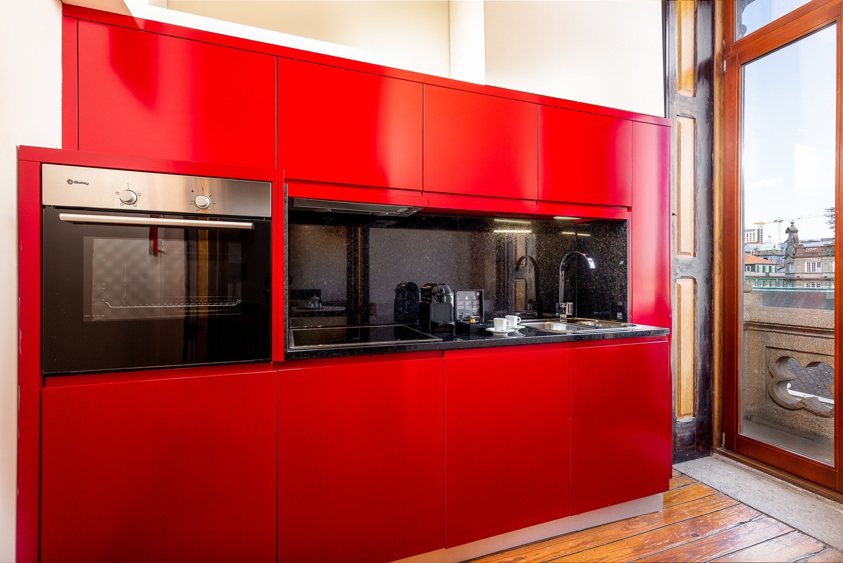 A modern kitchen with red cabinetry, a built-in oven, and a window with a city view.