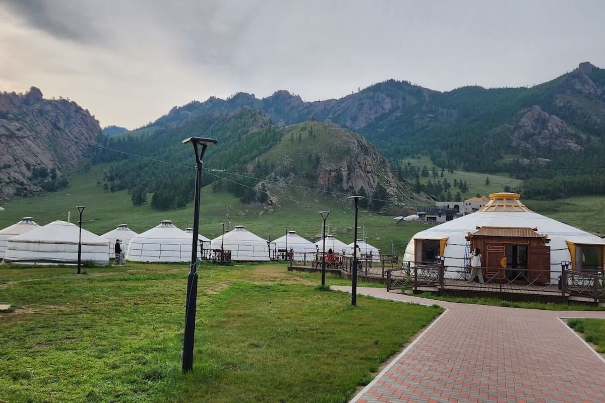 Yurts in a grassy field with mountains in the background.