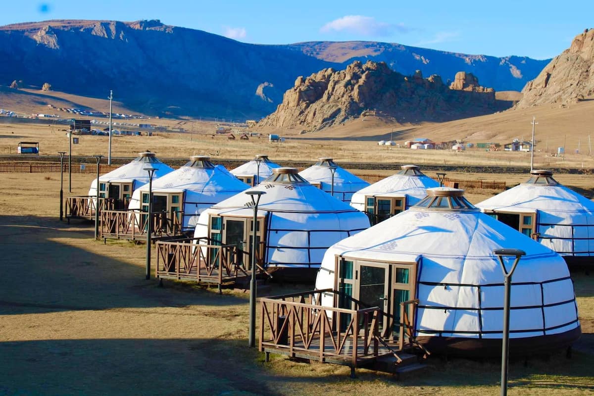 Yurts arranged in a row with wooden walkways, set against a mountainous backdrop.