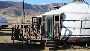 A yurt with a wooden entrance and a metal door, set in a grassy field with mountains in the background. - Khumug Tour Resort (Ulaanbaatar)