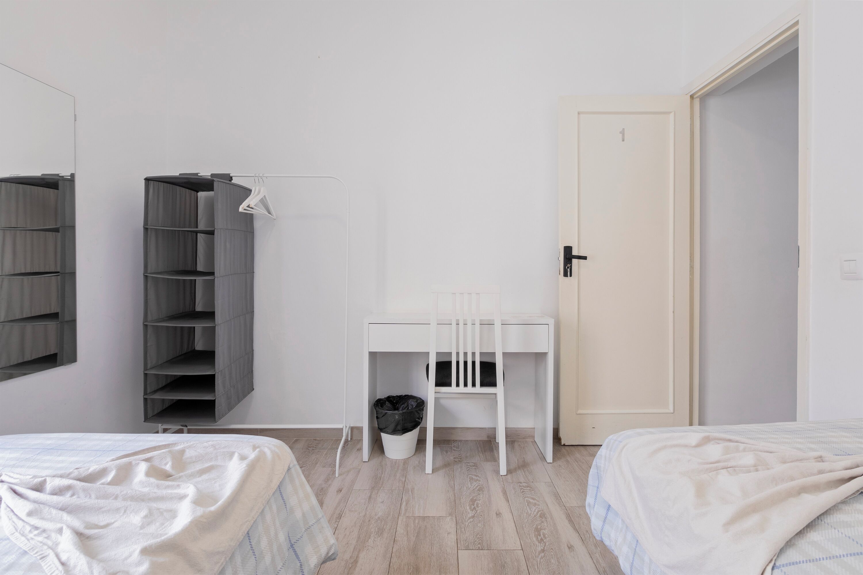 Un dormitorio con dos camas, un escritorio, una silla, un armario y una puerta.