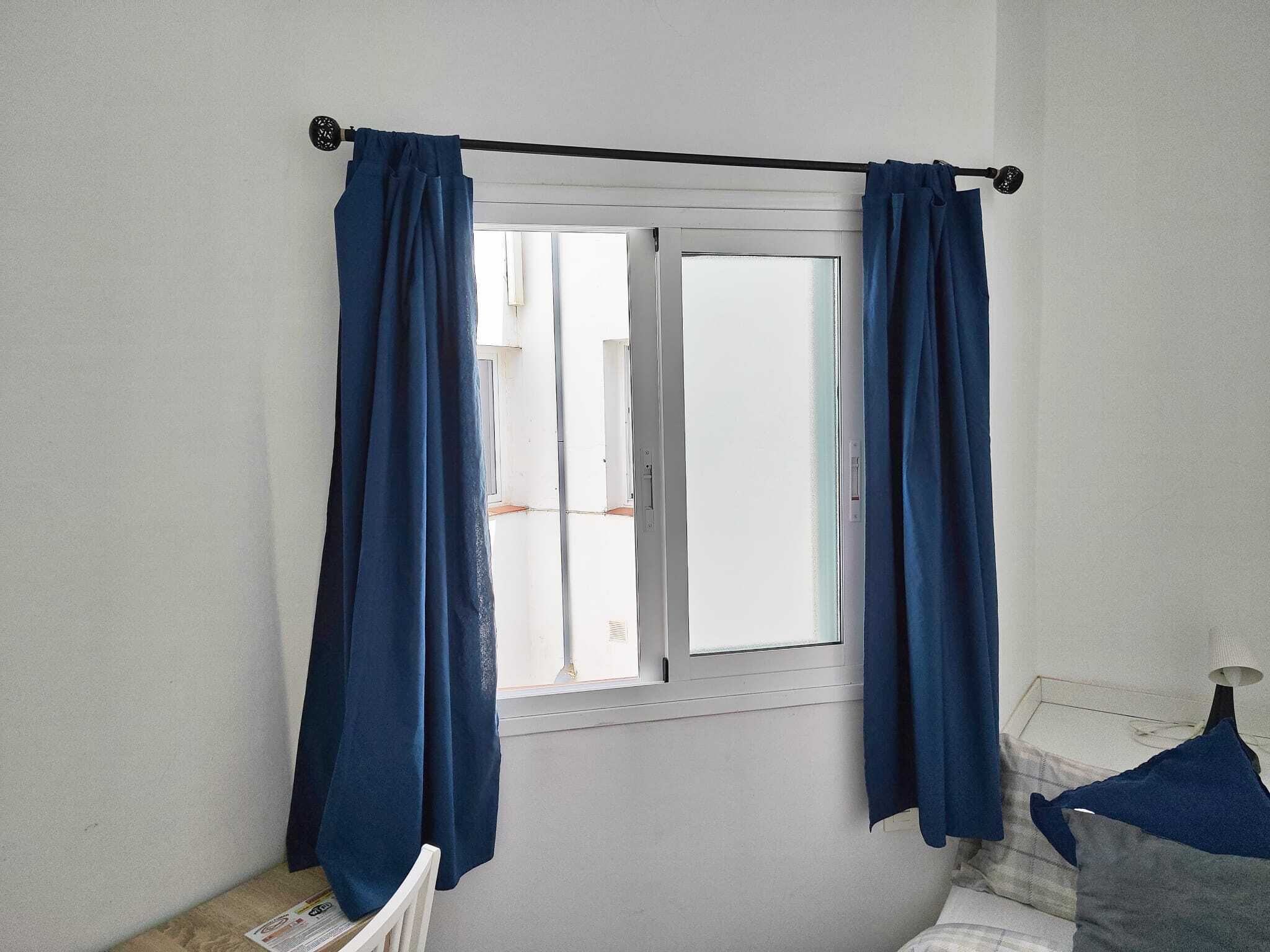 Een kamer met een raam, witte muren en een bed met een wit hoofdeinde.