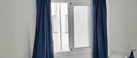 Een kamer met een raam, witte muren en een bed met een wit hoofdeinde.