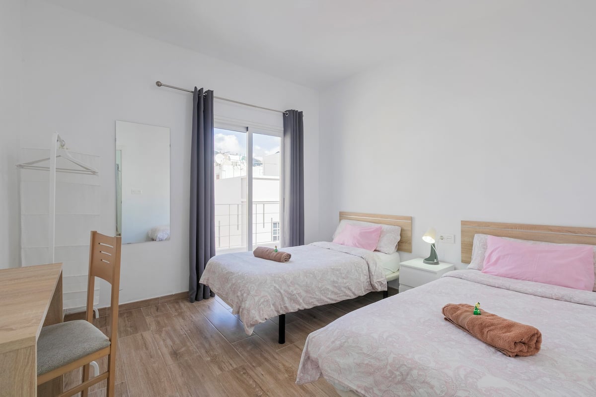 A room with two beds, a wooden chair, a desk, and a window with curtains.