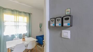 A room with a dining table, chairs, a blue sofa, a cactus on the wall, and a door with a lock and a light switch.