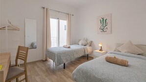A bedroom with two beds, a desk, a chair, a nightstand with a lamp, and a window with curtains. - TENERIFE URBAN ROOMS (Santa Cruz de Tenerife)