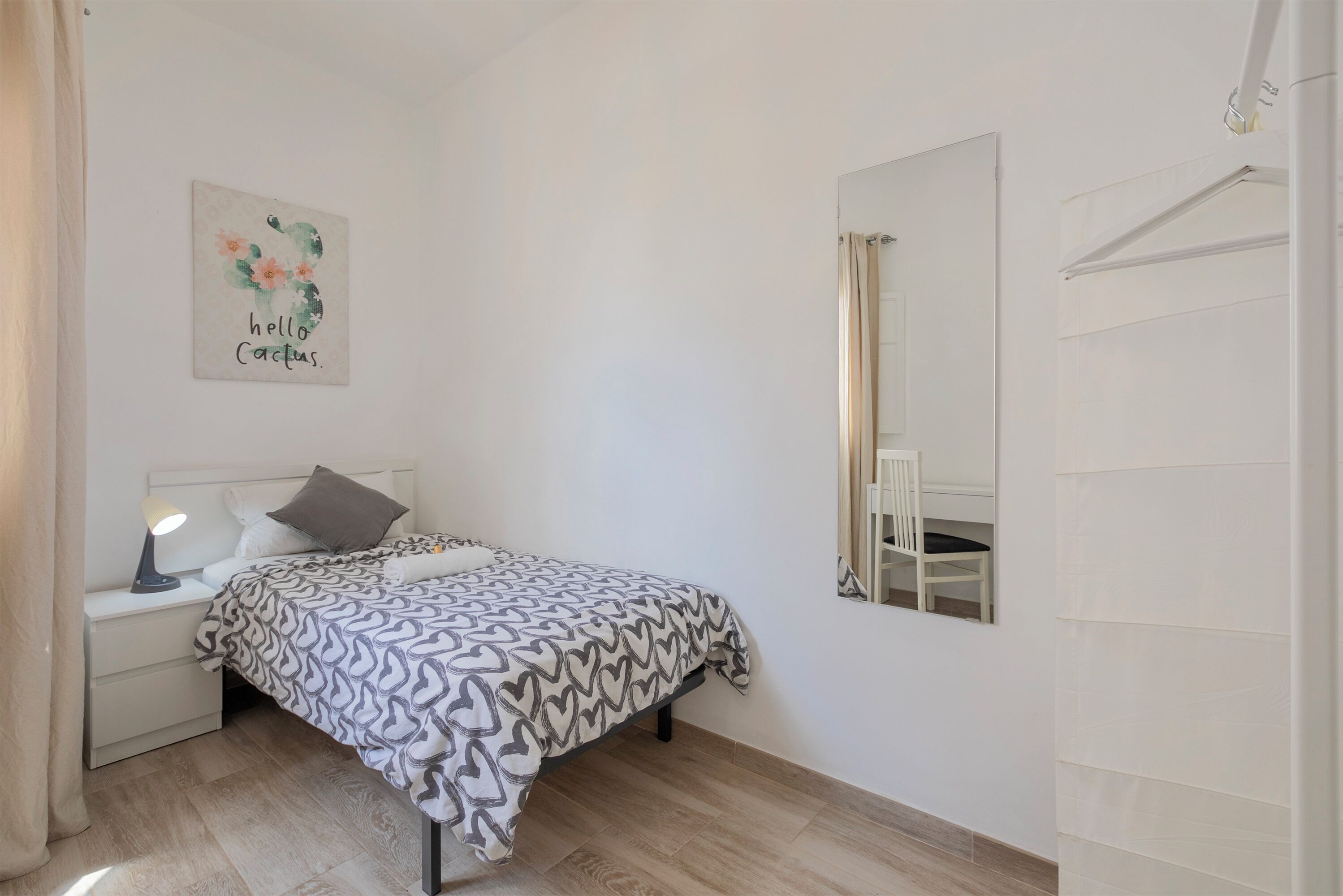 Quarto com cama, mesa de cabeceira, luminária e espelho fixado na parede.