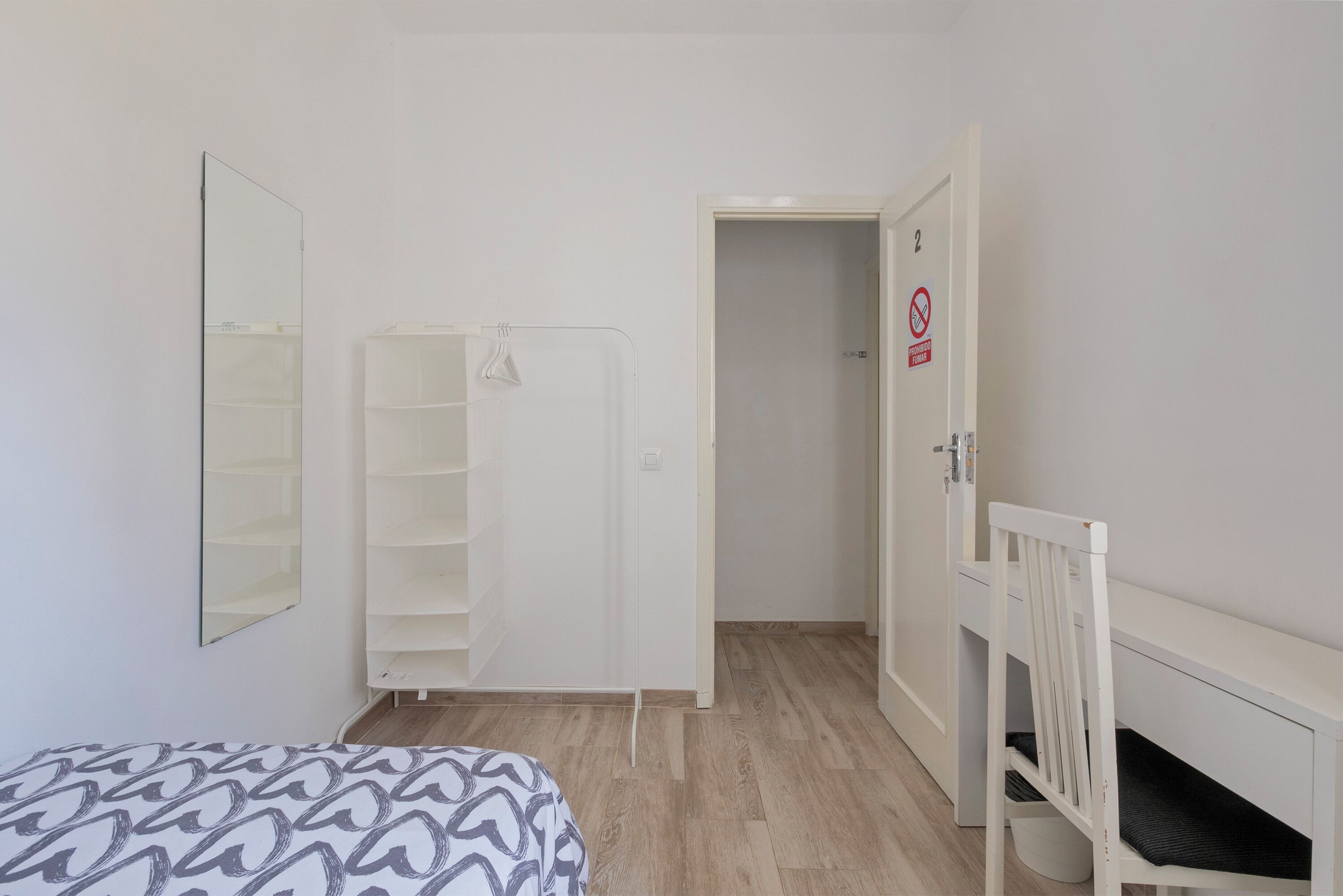 A bedroom with a bed, a wardrobe, a chair, and a door with a number.