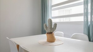 A white table with a woven cactus centerpiece, a white chair, and a window with curtains. - TENERIFE URBAN ROOMS (Santa Cruz de Tenerife)