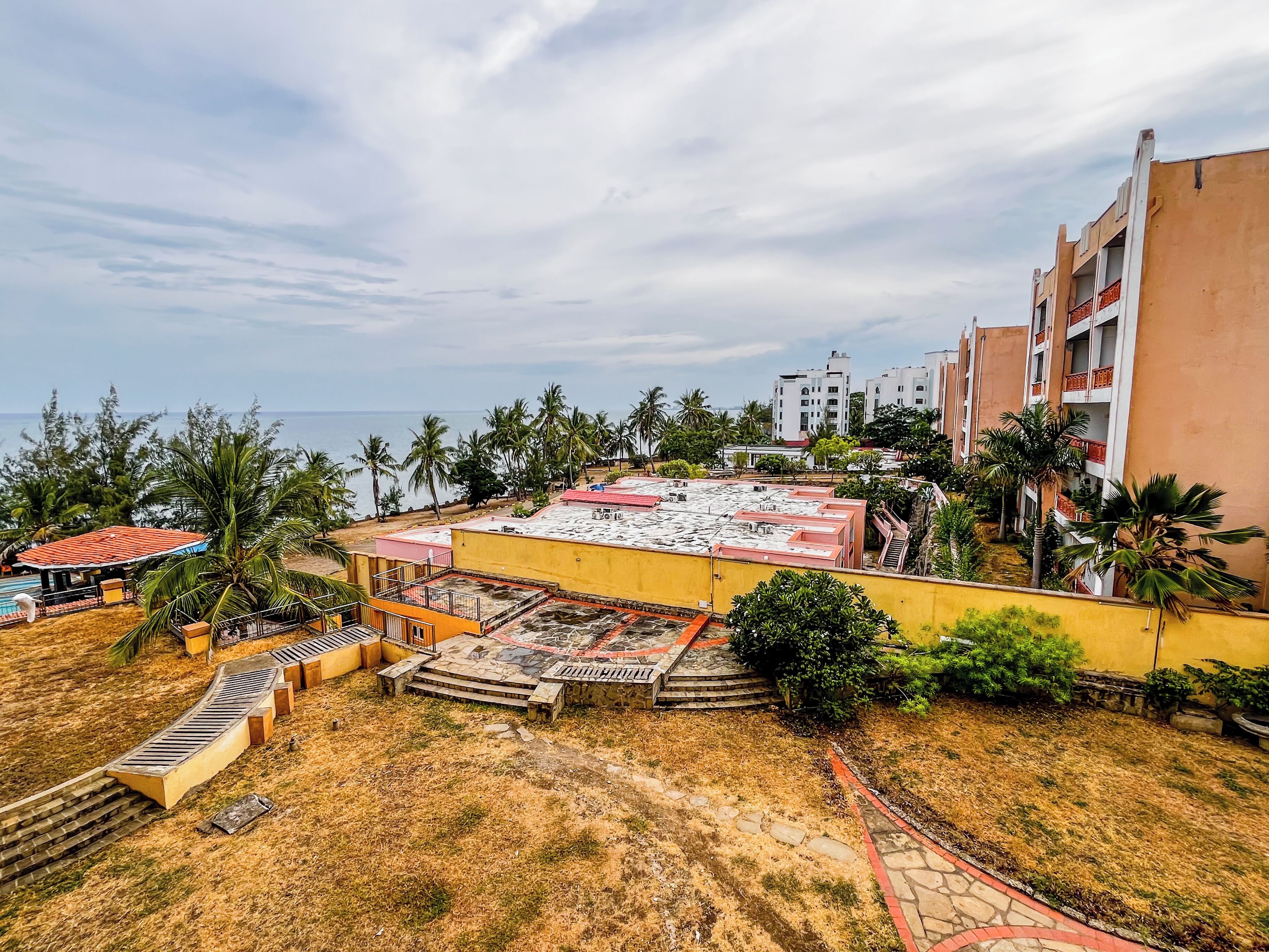 Un hotel con piscina en la azotea, palmeras y vistas al océano.