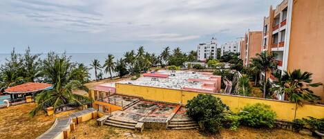 Un hotel con piscina en la azotea, palmeras y vistas al océano.