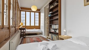 Un dormitorio con cama, escritorio con lámpara, estantería y ventana con vistas.