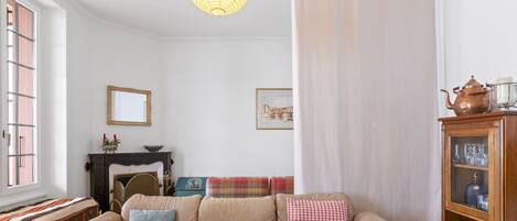 A cozy living room with a sofa, a fireplace, a window, and a cabinet with glassware.