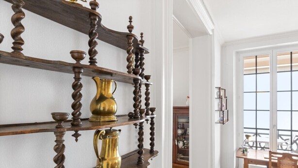 Una habitación con una repisa de madera en la pared, que sostiene jarras y cuencos de latón.