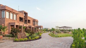 A modern building with a stone facade, a curved pathway, and a garden area. - Govind Bagh Resort (Jodhpur)