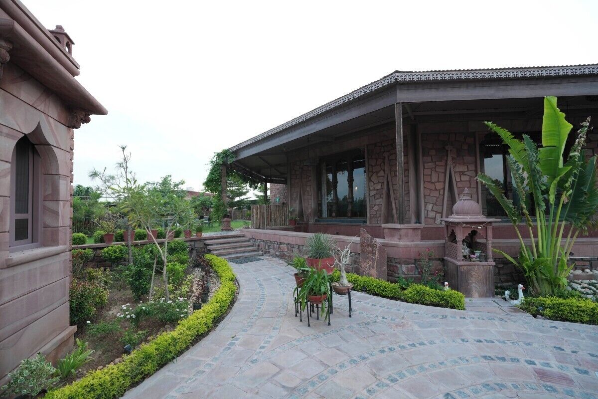 Ein traditionelles Gebäude mit einer Steinaußenfassade, einer überdachten Terrasse mit gewundenem Weg und einem kleinen Garten mit Blumentöpfen und einer Zierbrunnen.