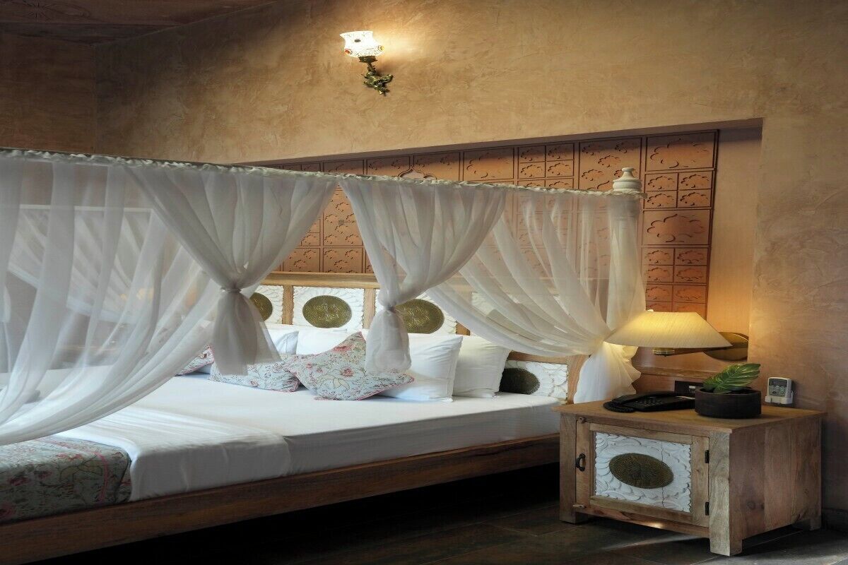 A bedroom with a bed, white curtains, a bedside lamp, and a nightstand.