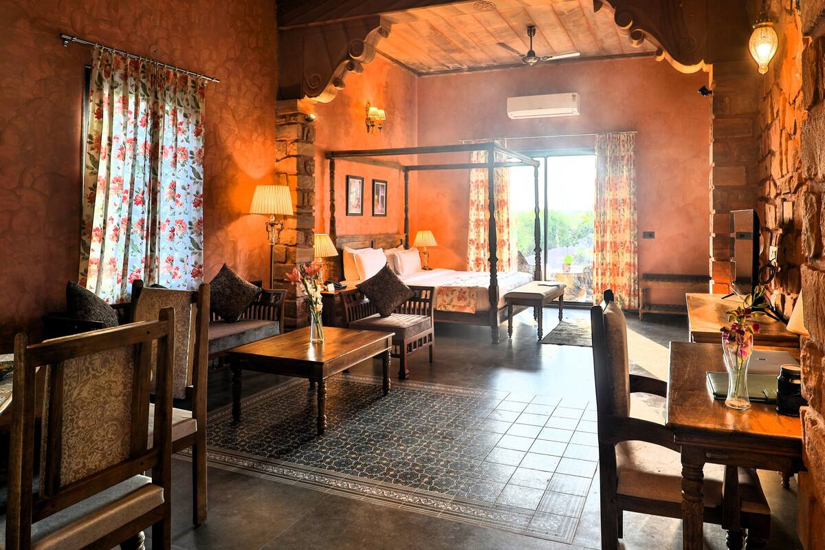 A room with a four-poster bed, wooden furniture, a stone wall, and a view through a window.