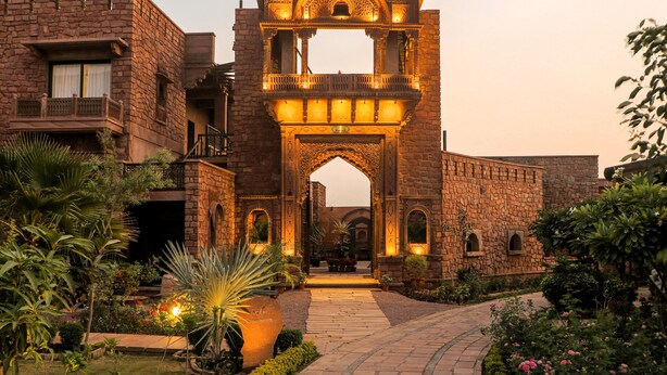 A stone building with an ornate archway, a pathway, and a garden with various plants.