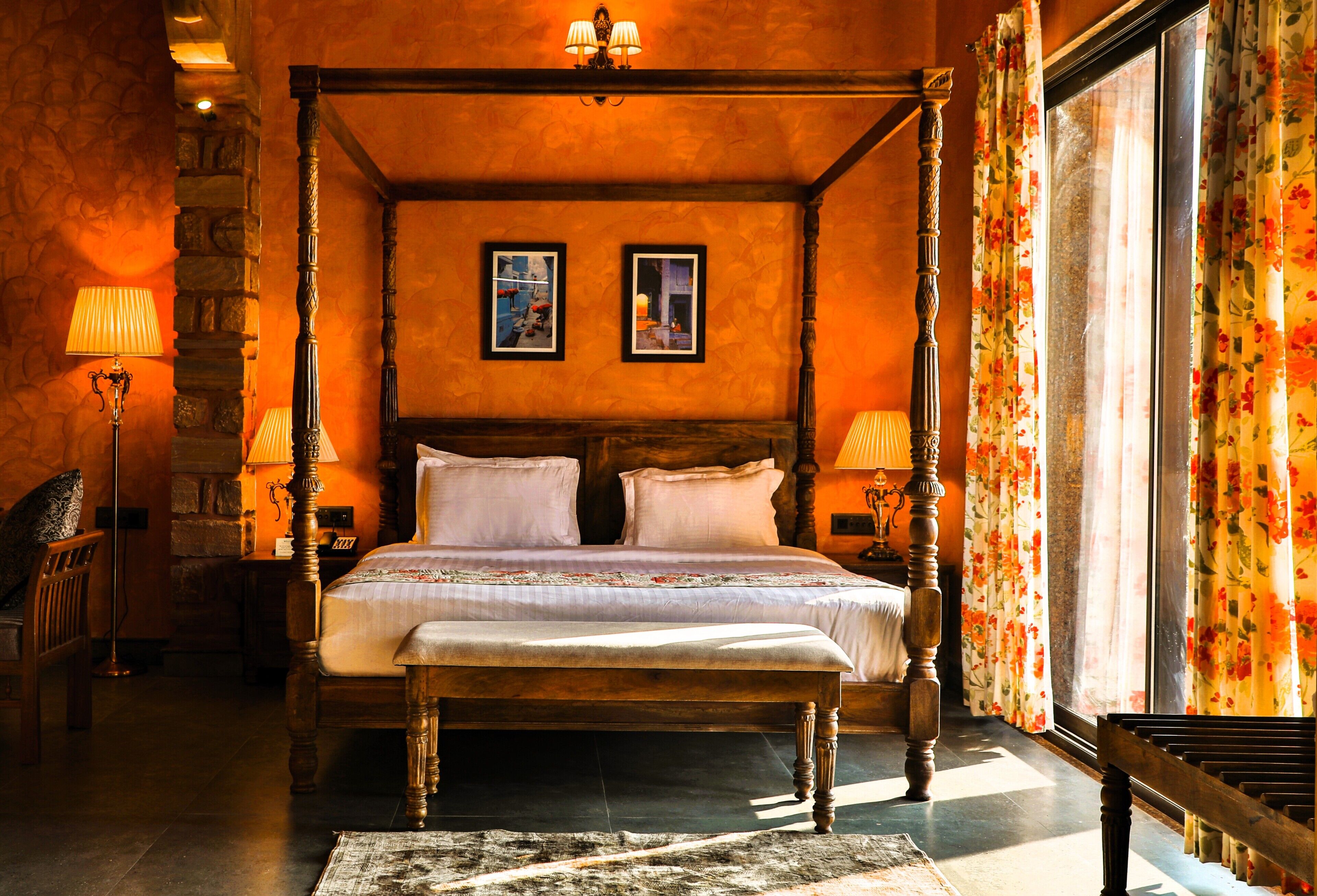 Un lit à baldaquin avec une tête de lit, deux tables de chevet, un banc, un tapis et un mur en pierre.
