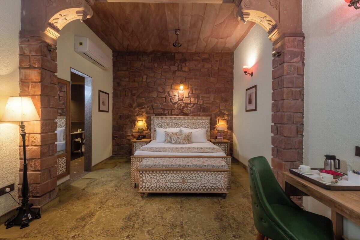 A bedroom with a stone wall, a bed with patterned bedding, two bedside lamps, and a wooden table with a tray.