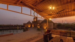 An outdoor seating area with a wooden table and chairs, a pool, and a building with domed structures in the background.