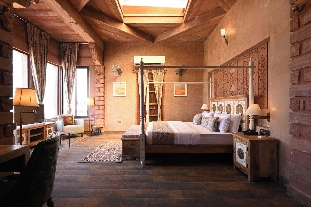 A cozy bedroom with a large bed, a wooden desk, a chair, and a ladder against the wall.