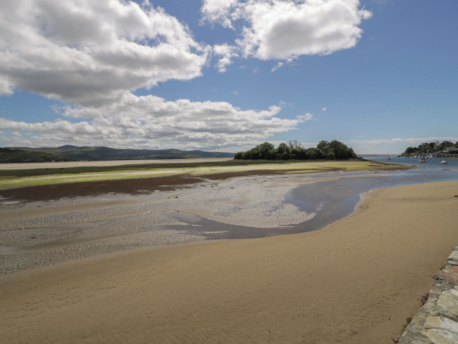 A beach with a sandy shore, a small island with trees, and a clear sky with clouds.