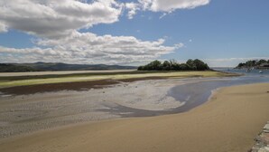 A beach with a sandy shore, a small island with trees, and a clear sky with clouds. - Lan y Mor (Porthmadog)