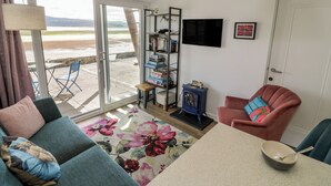 A living room with a sofa, a chair, a coffee table, a bookshelf, and a TV. - Lan y Mor (Porthmadog)