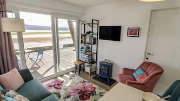 Una sala de estar con un sofá, una silla, una mesita de centro, una estantería y un televisor.