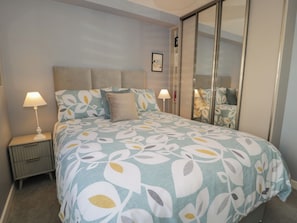 A bedroom with a bed, two bedside tables, a nightstand, a mirror, and a framed picture on the wall.