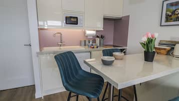 Una cocina moderna con armarios blancos, microondas integrado, un lavamanos y un comedor con dos sillas y una mesa.