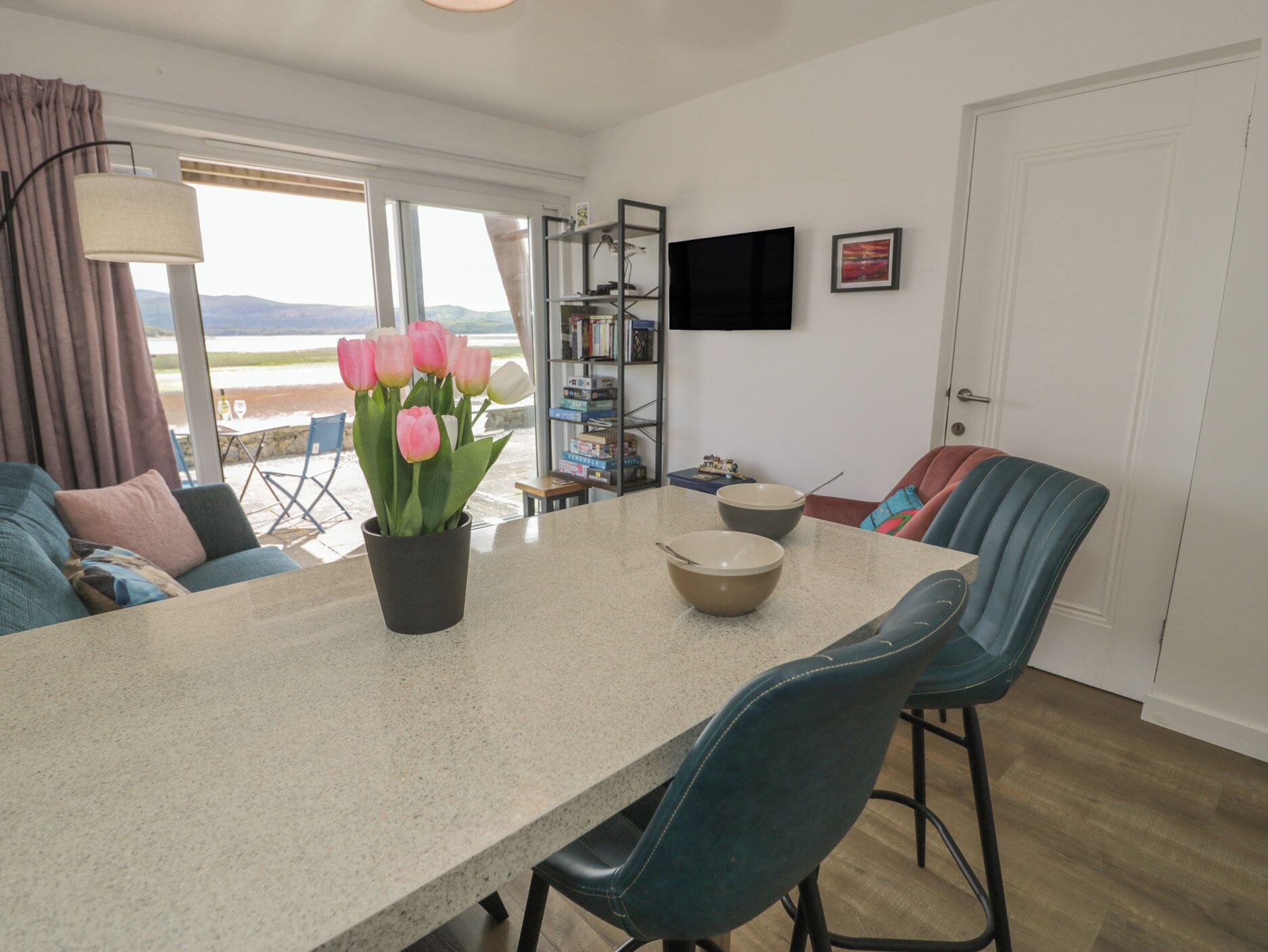 A modern kitchen with a dining table, chairs, a potted plant, and a TV mounted on the wall.