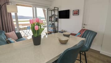 Eine moderne Küche mit Esstisch, Stühlen, einem Topfblumen und einem an der Wand befestigten Fernseher.