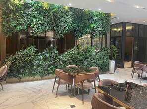 A modern interior with a dining area featuring a glass-top table and cushioned chairs, surrounded by lush green vertical gardens.