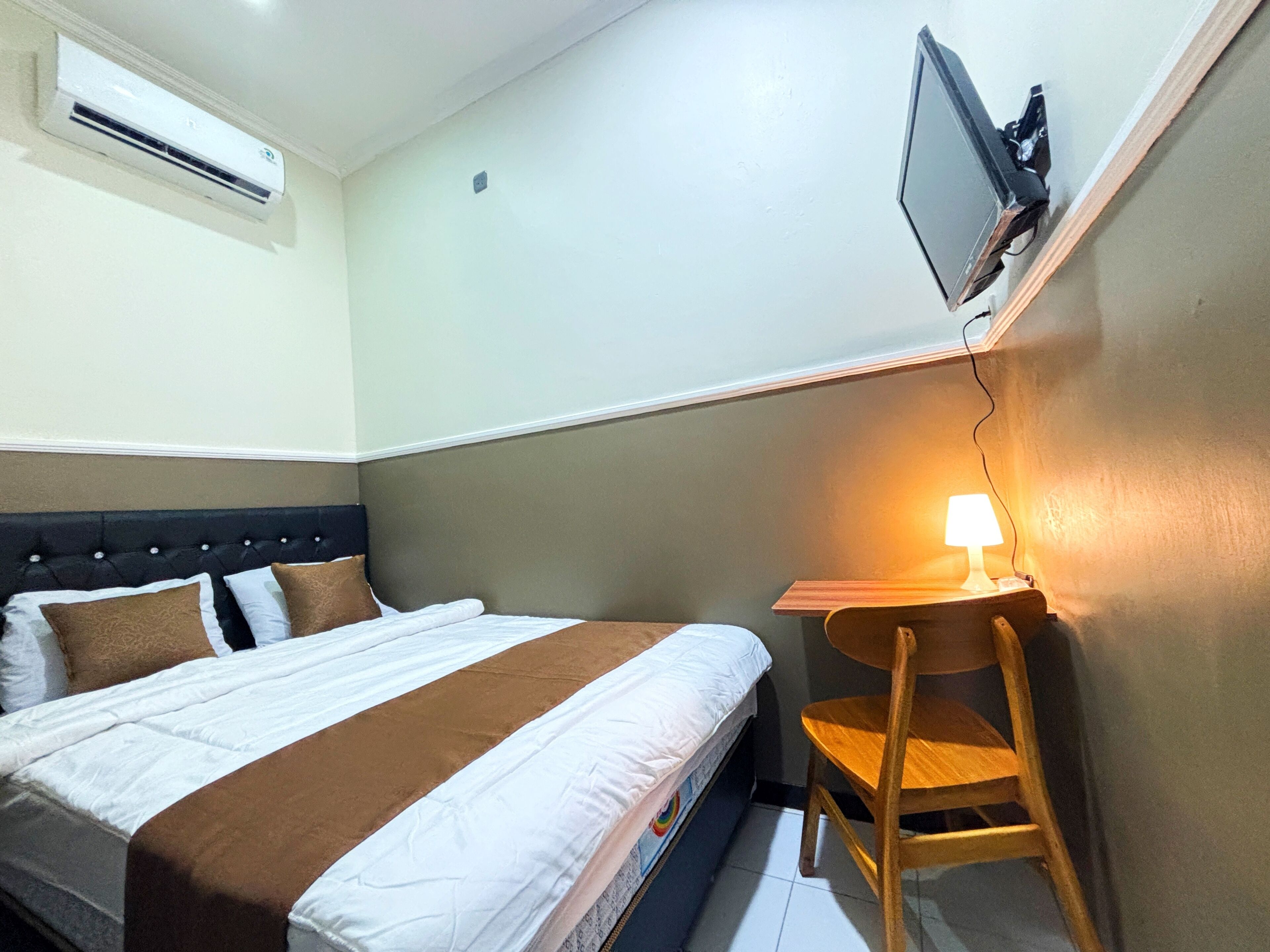 Een hotelkamer met een bed, een bureau, een stoel, een airconditioner en een televisie aan de muur.