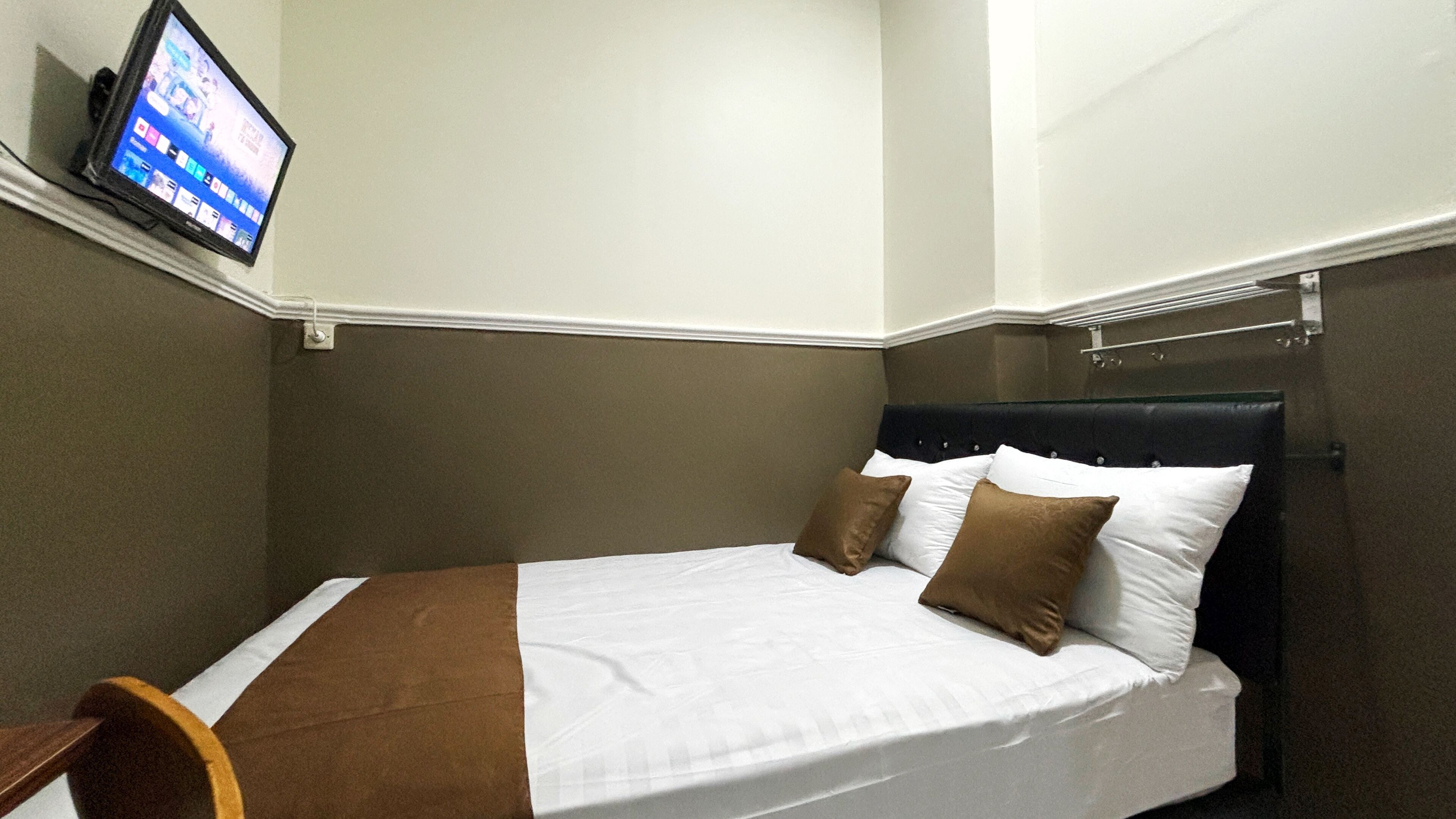 Una habitación de hotel con una cama individual, un televisor montado en la pared y una pequeña mesita de madera.