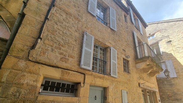 Un bâtiment en pierre avec une porte en métal, des volets et une petite fenêtre grillagée.