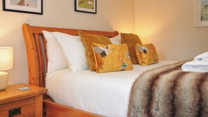 Een slaapkamer met een houten hoofdeinde, wit beddengoed en twee ingelijste foto's aan de muur.