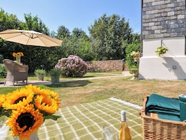 Un patio con mantel a cuadros, una silla de mimbre, una sombrilla y una maceta con flores moradas.
