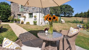 Een terras met rieten meubels, een glazen tafel en een vaas met zonnebloemen.