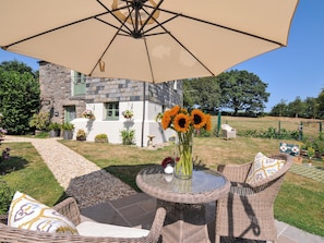 A patio with wicker furniture, a glass table, and a vase with sunflowers. - The Mill (Lostwithiel)