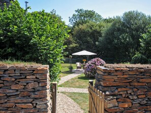 A stone wall entrance to a garden with a pathway leading to a seating area under an umbrella. - The Mill (Lostwithiel)